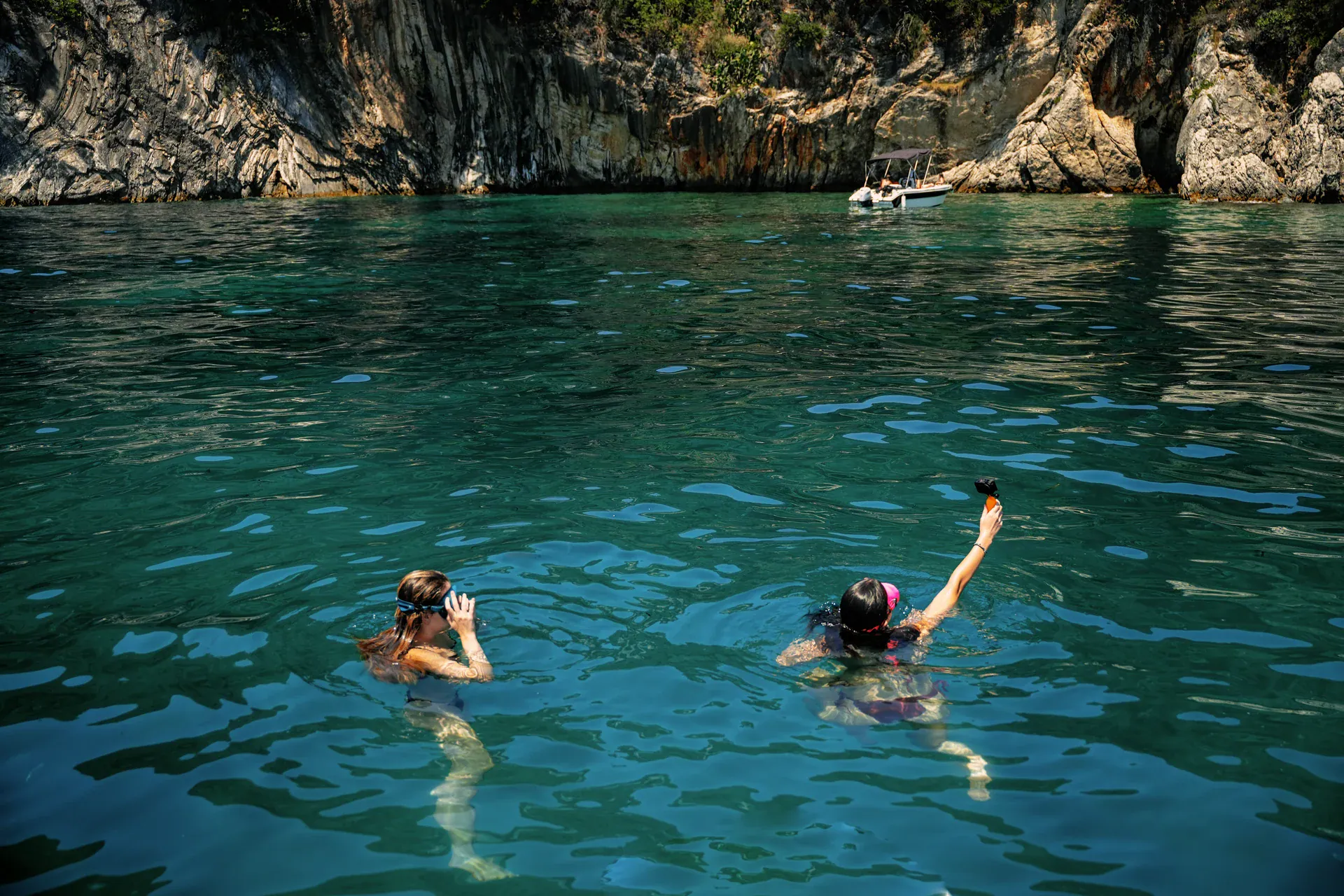 Two people swimming in clear water beside a rocky cove