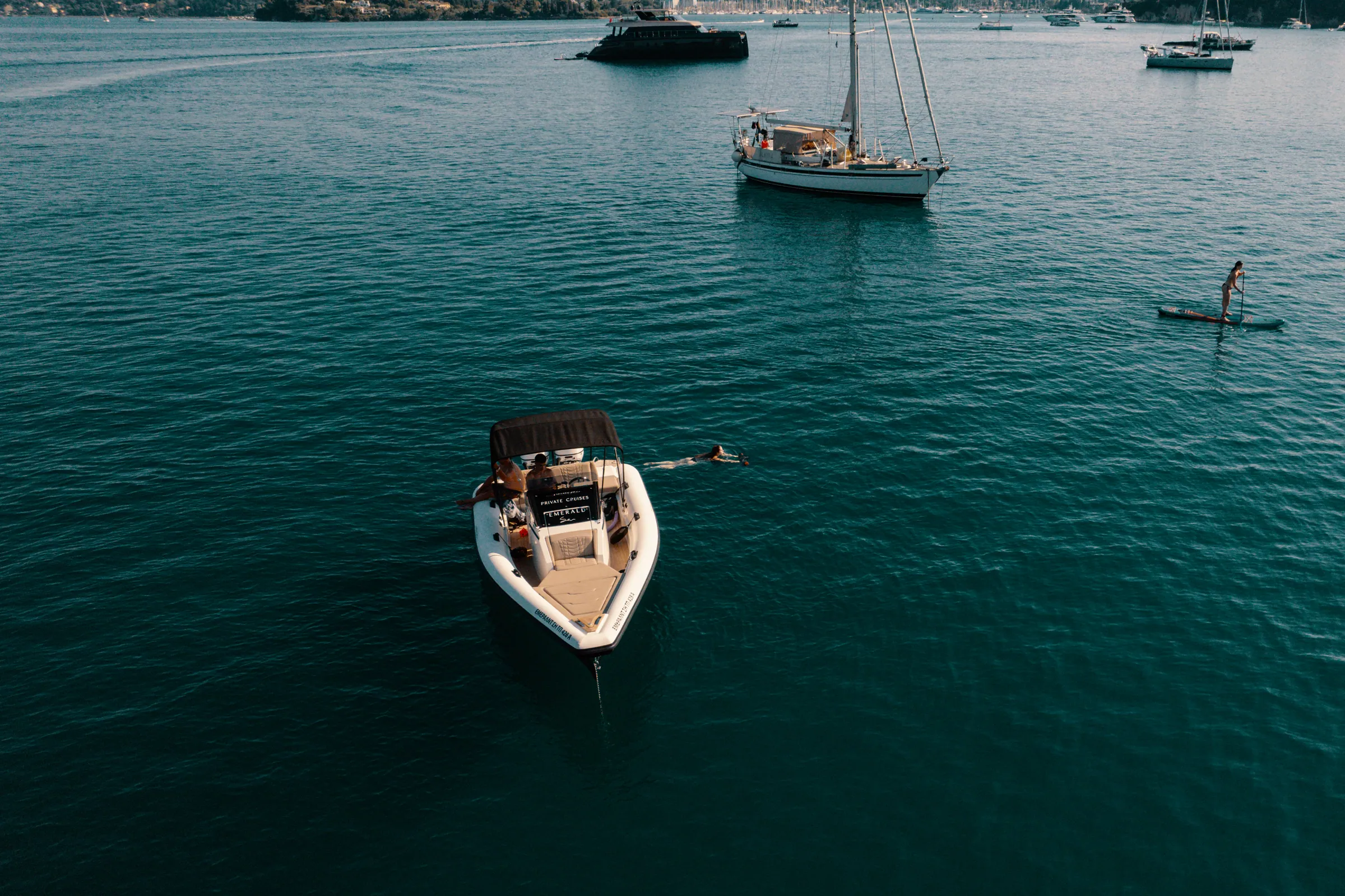Emerald at anchor in a sheltered northeast Corfu bay, with a guest swimming alongside and a paddleboard nearby