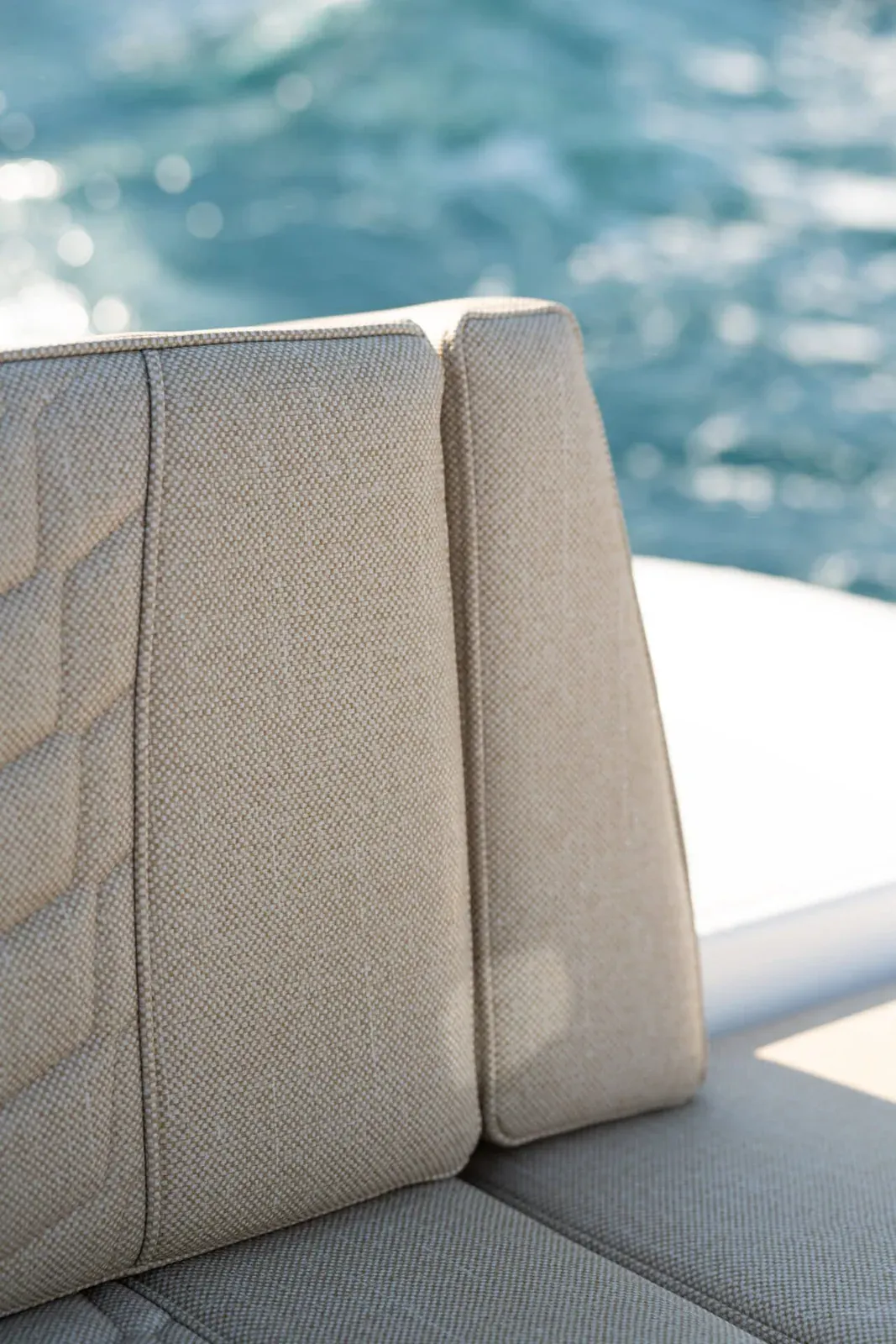 A corner of the rear bench in quilted upholstery with the white gunwale beside it and open water behind