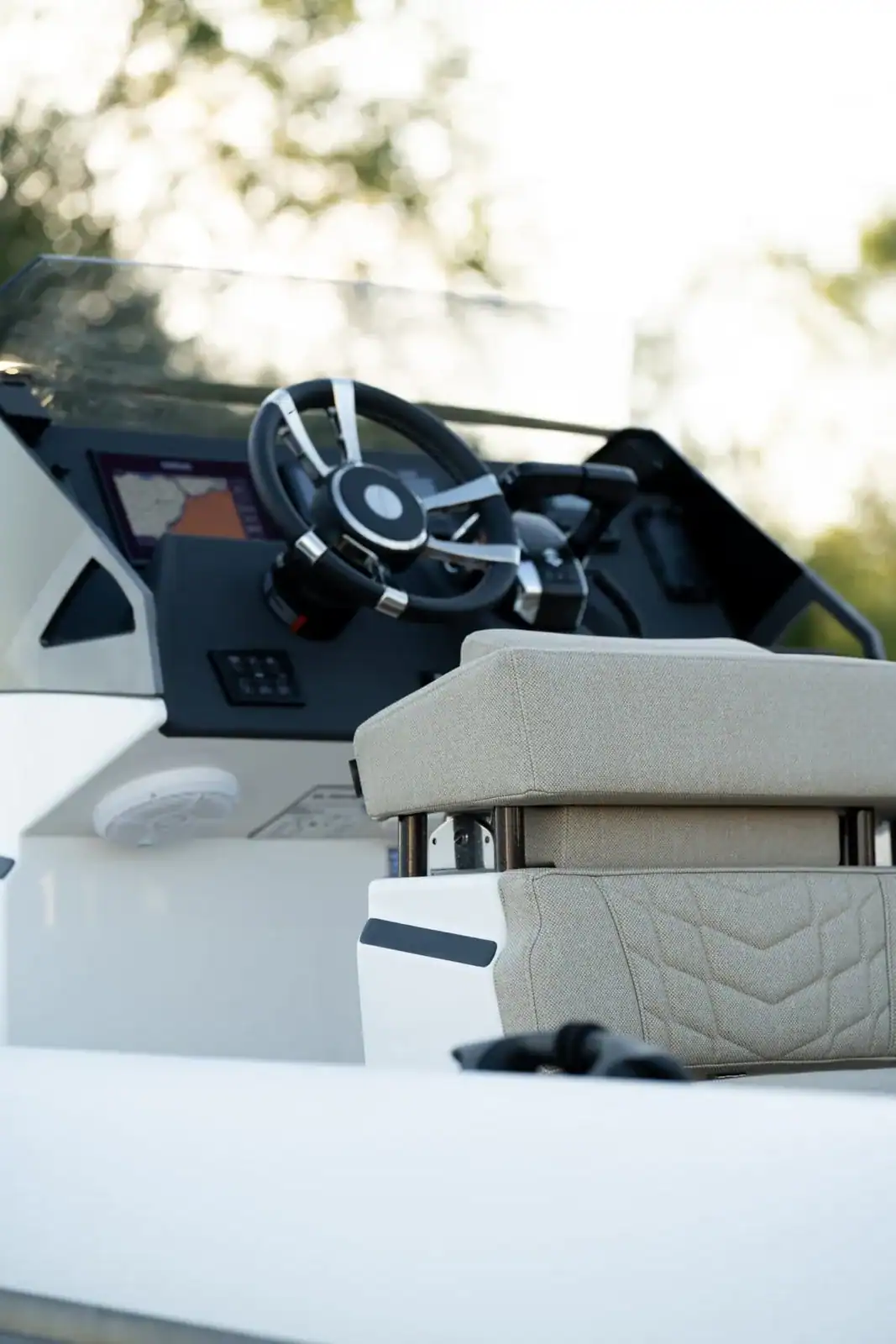 The helm console seen from the side with the quilted helm seat beside it and shore greenery behind