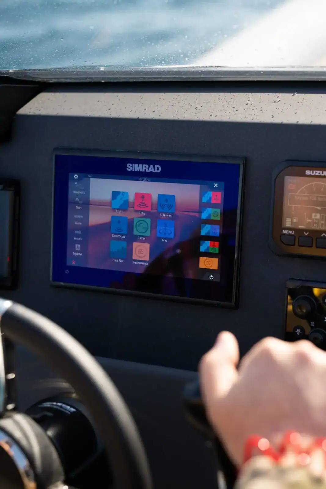 A hand resting on the steering wheel with the lit chartplotter and a gauge alongside